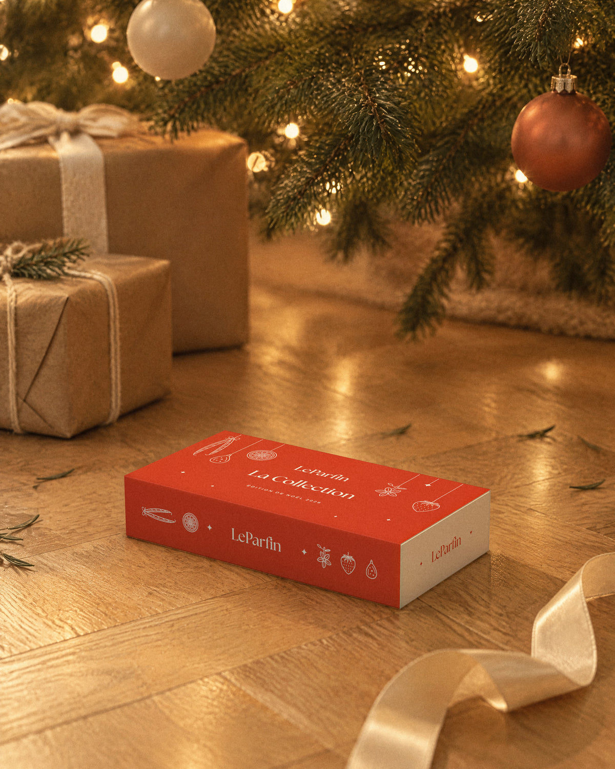 Le coffret La Collection posé sous un sapin, entre des paquets en papier kraft.