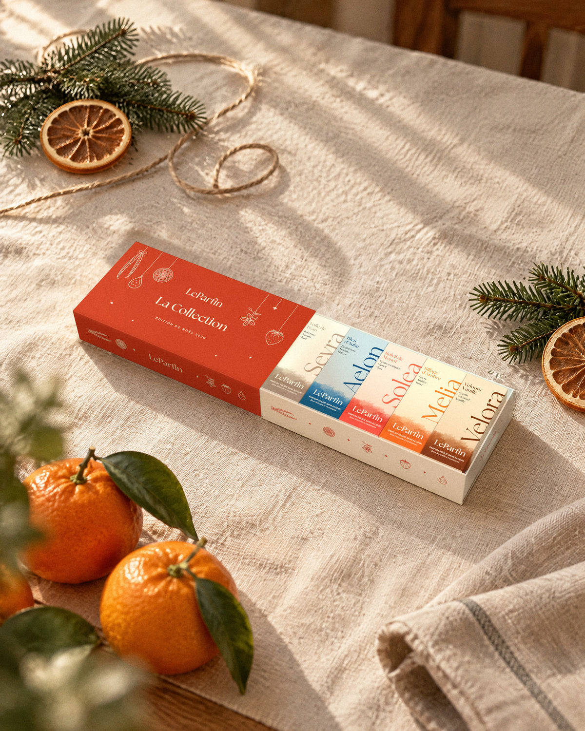 Le coffret ouvert sur une table de fête, entre des branches de sapin et des oranges séchées.